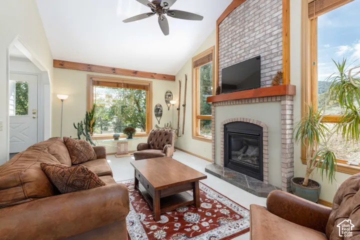Vaulted ceiling, exposed wood beams, brick-surround fireplace with hearth, wood-framed windows, and a ceiling fan