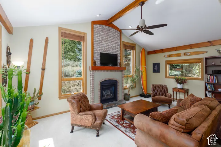 Vaulted ceiling with exposed wood beams, brick fireplace with a stone hearth, natural wood-framed windows, and built-in shelving