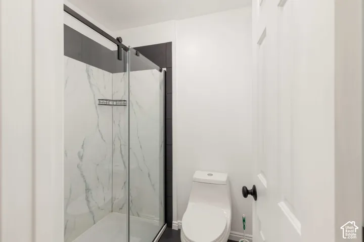 Glass-enclosed shower with a sliding barn door hardware system, marble-look paneling, and contrasting dark wall tiles