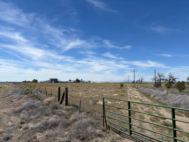 Expansive land parcel featuring a wire fence, green metal gate, and a dirt road
