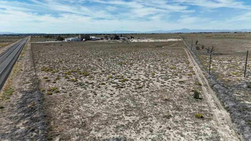Expansive land parcel featuring a paved road, dirt access path, and distant structures