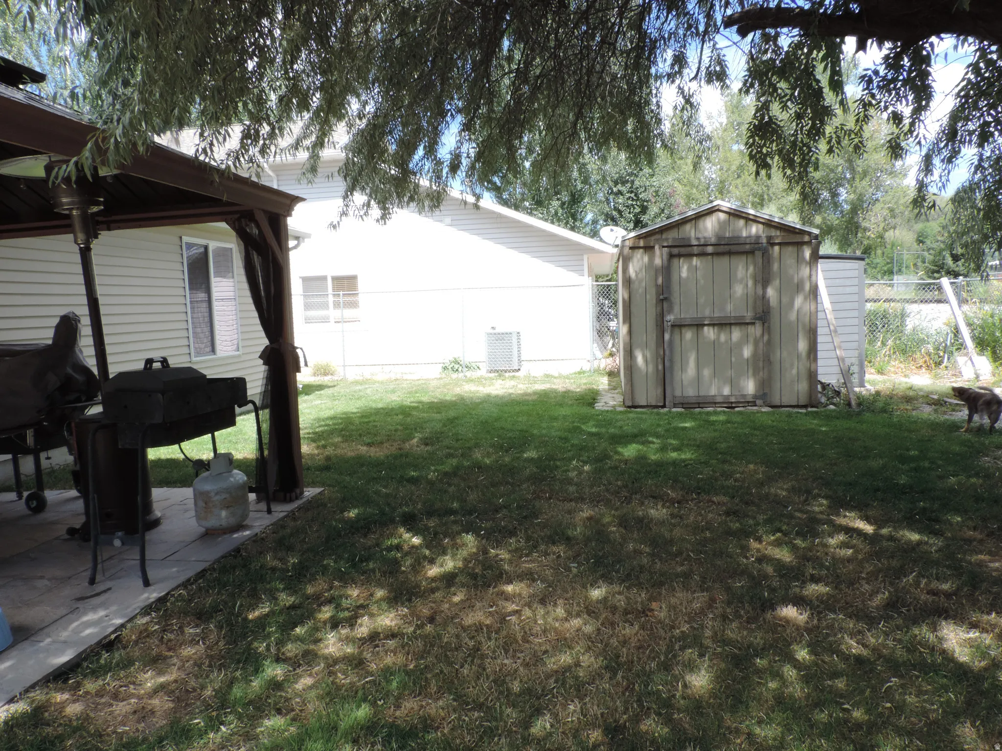 Spacious backyard with a shaded patio, permanent storage shed, and mature trees