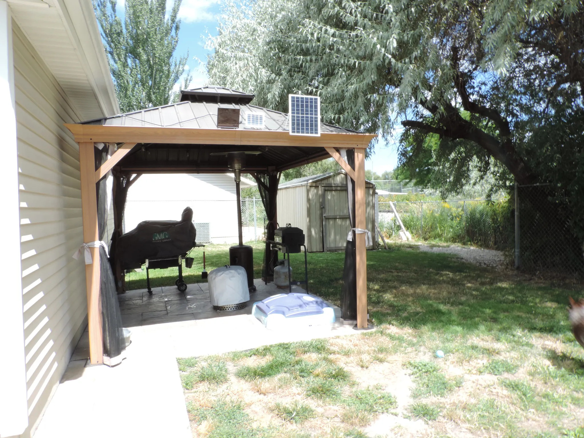Outdoor gazebo with a solar panel, paved patio, and a chain-link fence