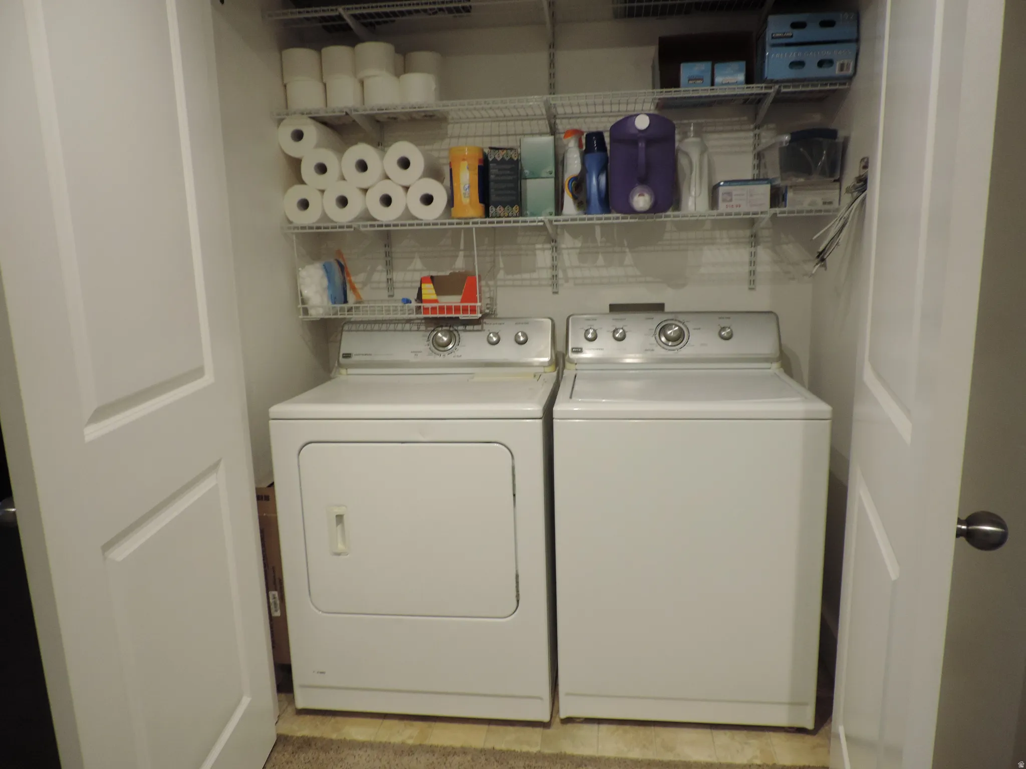 Laundry closet with white bi-fold doors, white wire shelving, and built-in appliances