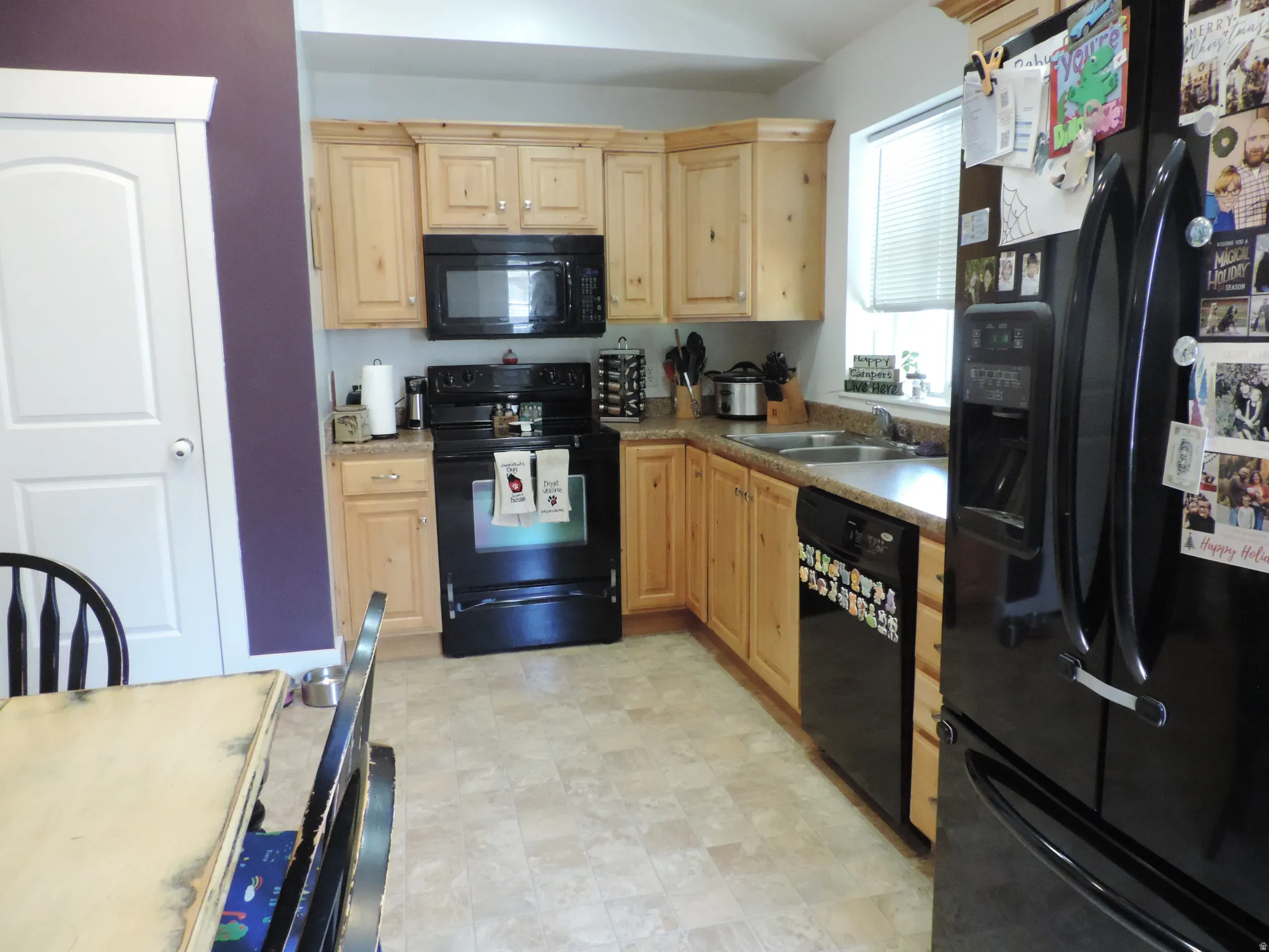 Kitchen featuring light wood cabinetry, a double basin sink, and a black appliance package including an oven and refrigerator
