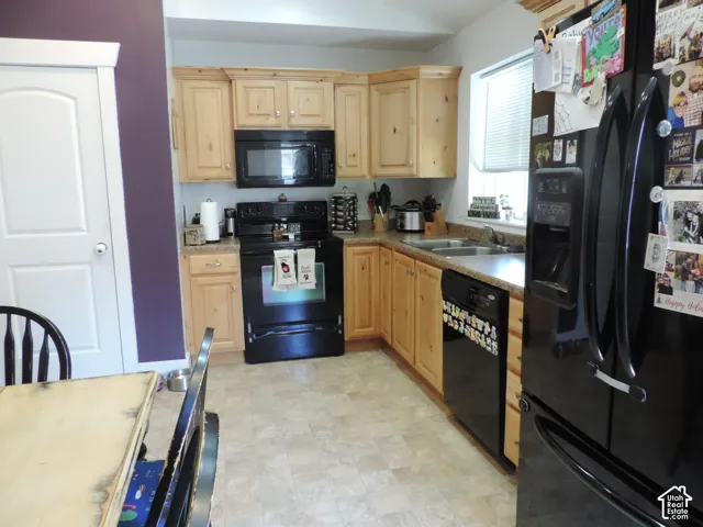 Kitchen featuring light wood cabinetry, a double basin sink, and a black appliance package including an oven and refrigerator