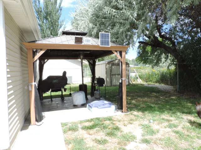 Outdoor gazebo with a solar panel, paved patio, and a chain-link fence