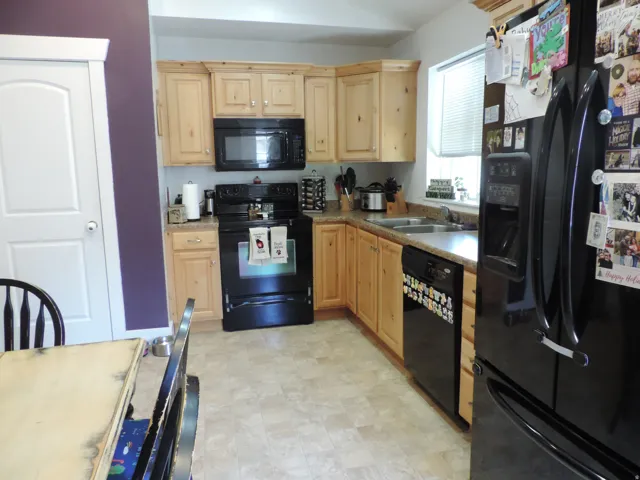 Kitchen featuring light wood cabinetry, a double basin sink, and a black appliance package including an oven and refrigerator
