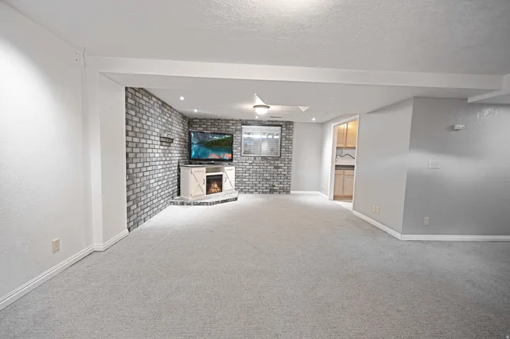 Spacious room featuring light gray carpeting, a decorative brick accent wall, recessed lighting, and a built-in electric fireplace with cabinetry