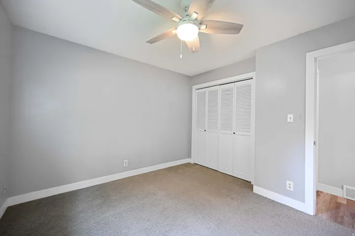 Light gray walls with white trim, a ceiling fan with integrated lighting, louvered bi-fold closet doors, and carpet flooring