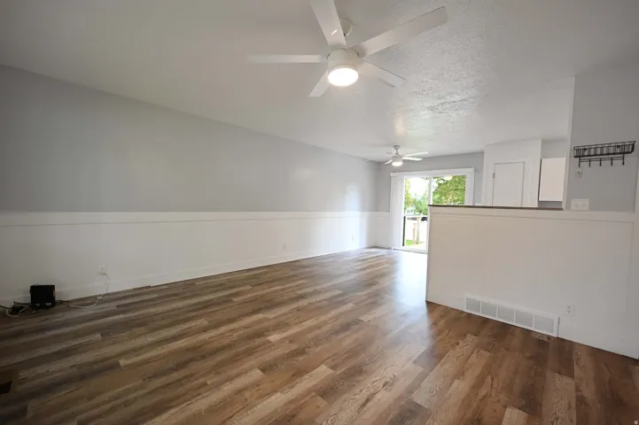 Wood-finish flooring throughout, white wainscoting, and a ceiling fan with integrated lighting