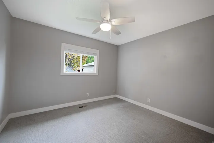 Carpeted flooring with a large window, white trim, and a ceiling fan