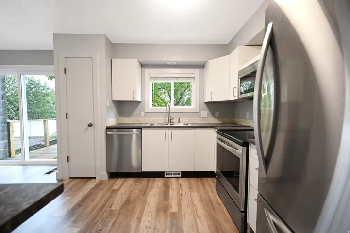 Kitchen featuring white cabinetry, dark countertops, stainless steel appliances, wood-finish flooring, and a sliding glass door