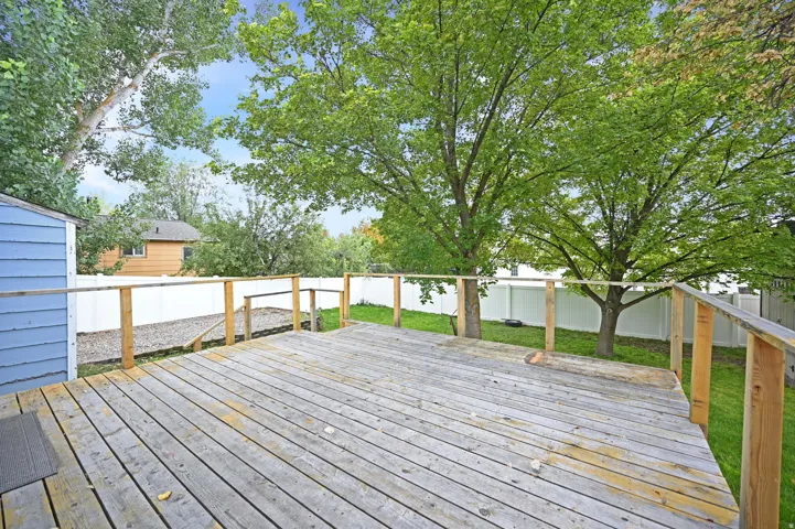 Expansive wood deck with a perimeter railing, overlooking a green lawn and mature trees