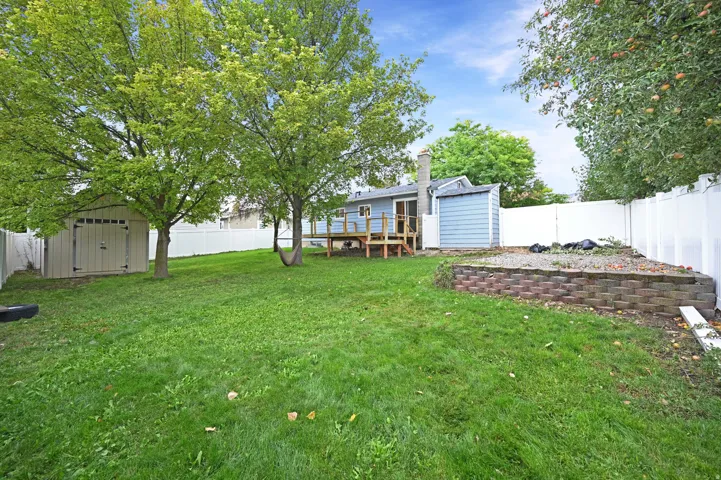 Expansive lawn with mature trees, a privacy fence, an elevated wood deck, a storage shed, and a raised garden bed