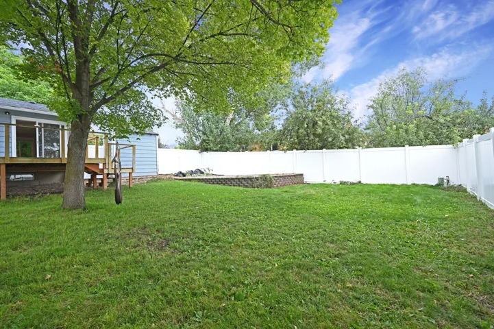 Expansive backyard featuring a manicured lawn, a white privacy fence, and a raised wood deck