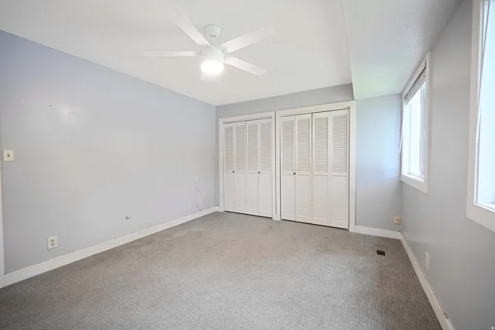 Ceiling fan with integrated lighting, two sets of bi-fold closet doors, wall-to-wall carpeting, and multiple windows