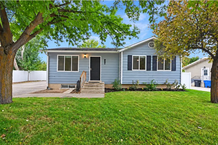 Light blue exterior siding with white trim, front lawn, and mature trees