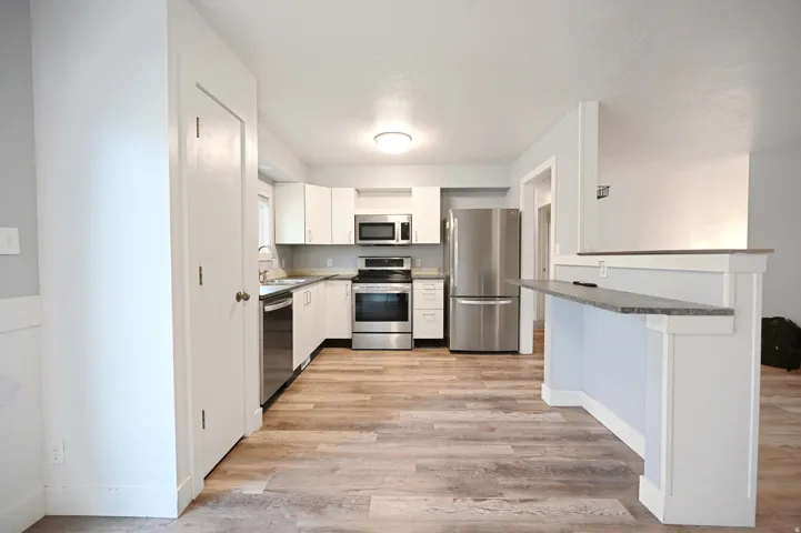 Kitchen featuring white cabinetry, stainless steel appliances, wood-finish flooring, a built-in pantry, and a breakfast bar with a stone-look countertop