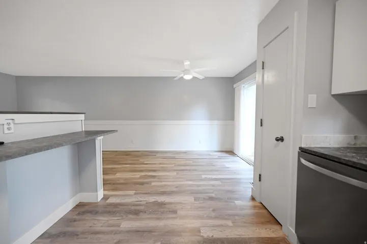 Open-concept layout with wood-finish flooring, wainscoting, and a ceiling fan