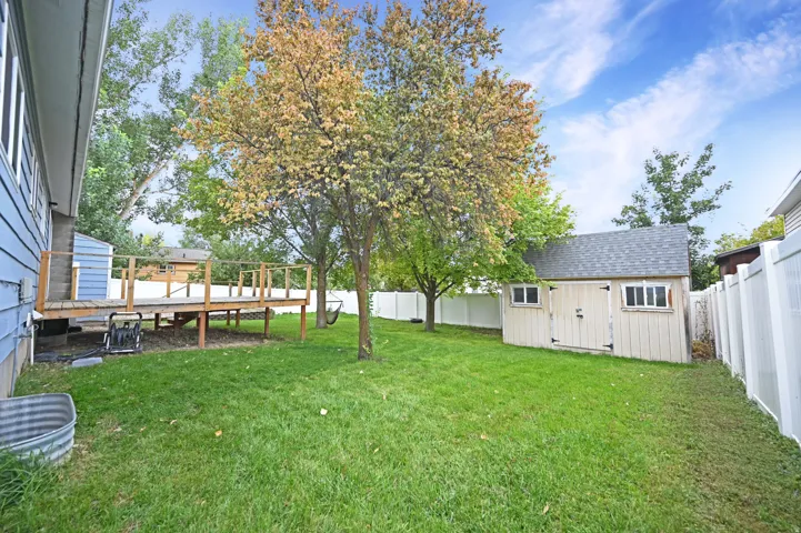 Expansive lawn area, multi-level wood deck, mature trees, white privacy fencing, and an outbuilding with an asphalt shingle roof