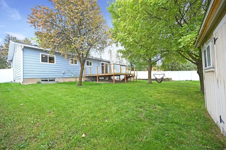 Expansive green lawn, elevated wooden deck, established trees, white privacy fencing, and blue siding