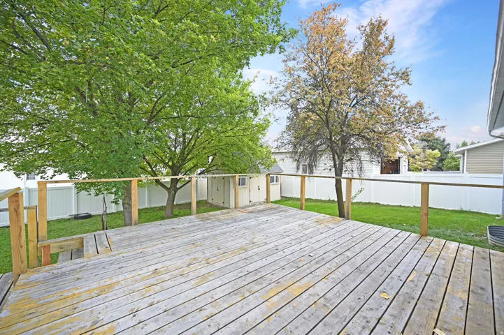 Expansive wood deck with wood railings, overlooking a fenced backyard with mature trees and a detached shed
