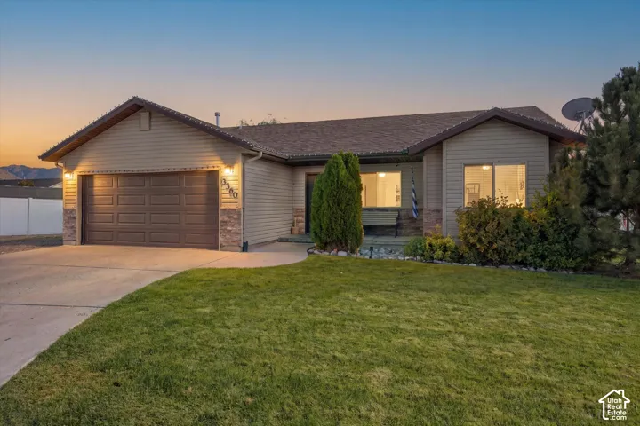 Single-story residence featuring a two-car garage, stone accents, and a front lawn with mature landscaping