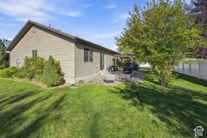Manicured lawn, mature trees, wood pergola, sliding glass door, and privacy fencing