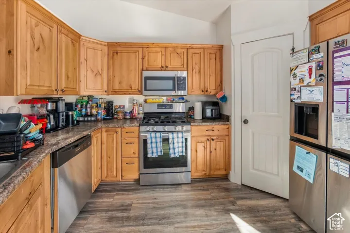 Kitchen featuring wood cabinetry, stainless steel appliances, laminate countertops, and wood-finish flooring