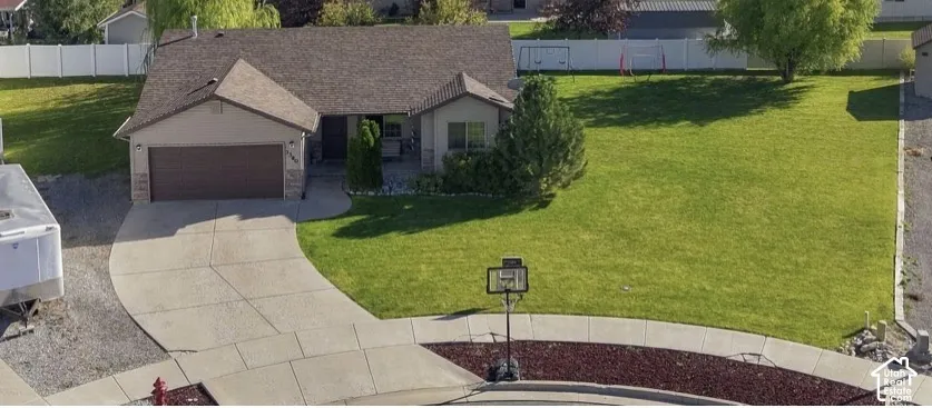 Single-story residence featuring a concrete driveway, two-car garage, and expansive lawn with white vinyl perimeter fencing