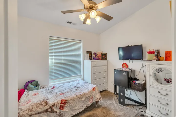 Vaulted ceiling, ceiling fan with integrated lighting, window with blinds, light-toned carpeting, neutral wall finishes