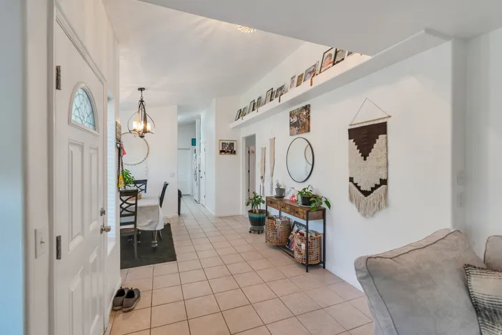 Entryway with tiled flooring, white panel door featuring an arched decorative glass insert, and a vaulted ceiling