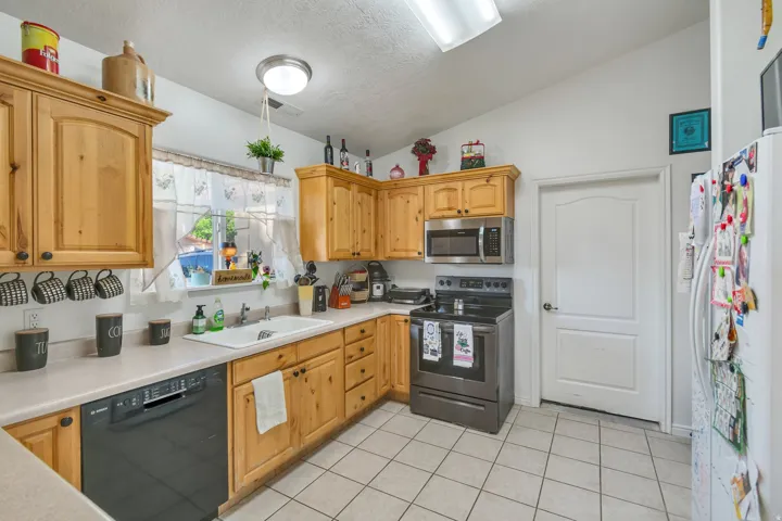Wood-finish cabinetry, stainless steel microwave, black range, white tile flooring, and a white paneled door
