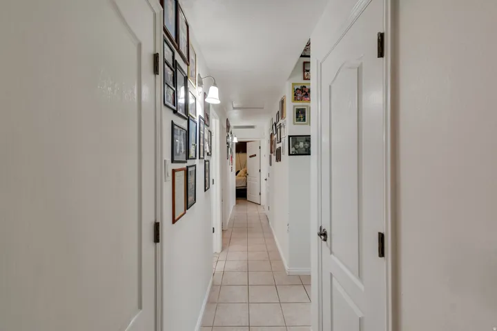 Recessed lighting illuminates the hallway, featuring light-toned tile flooring and white panel doors