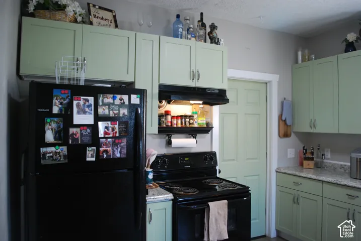 Kitchen featuring light green cabinetry, black range, and light gray countertops