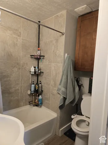Bathroom featuring a white bathtub, tiled shower surround, wood-finish flooring, and wall-mounted cabinetry