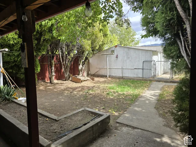 Covered patio area, concrete pathway, raised garden beds, wood fence, and mature trees