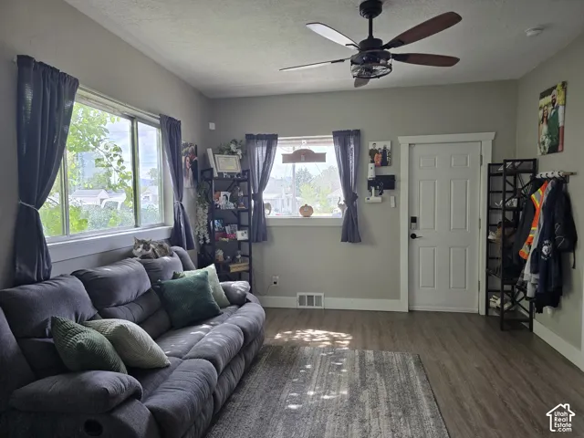 Wood-finish flooring, two large windows, ceiling fan with light fixture, and paneled interior door