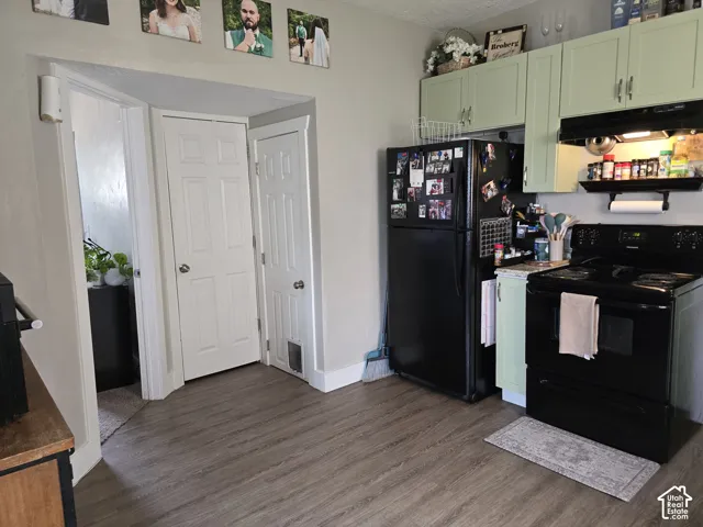 Kitchen featuring black appliances, light green cabinetry, and wood-finish flooring