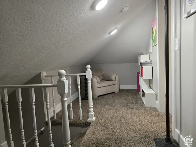 Sloped ceiling space featuring recessed lighting, a white painted railing, and textured carpet flooring