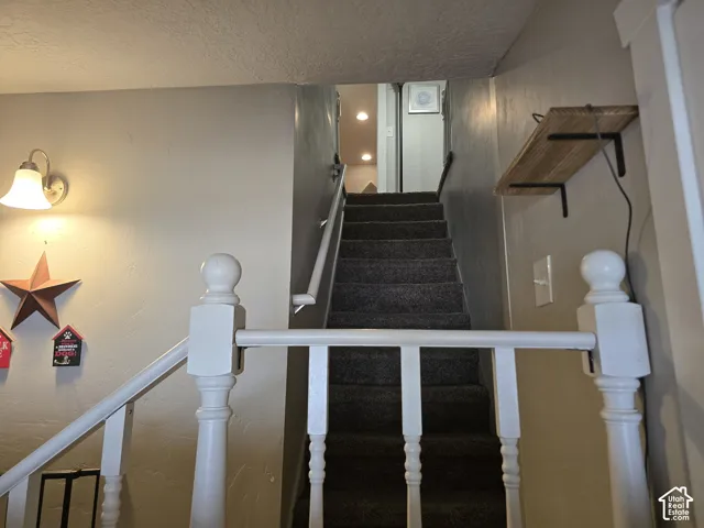 Carpeted staircase with white painted balusters and handrails, featuring a wall-mounted sconce and a built-in wall shelf