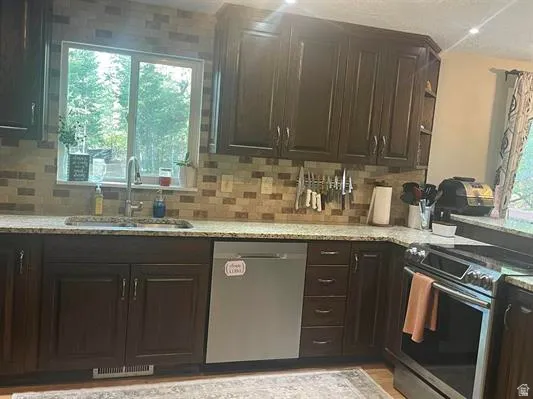 Dark wood cabinetry, stainless steel dishwasher, stainless steel range, light-toned backsplash, and light-toned countertops