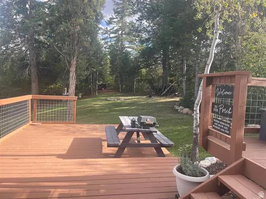 Expansive wood deck with wire grid railing, offering a generous outdoor living space overlooking a manicured lawn and mature trees