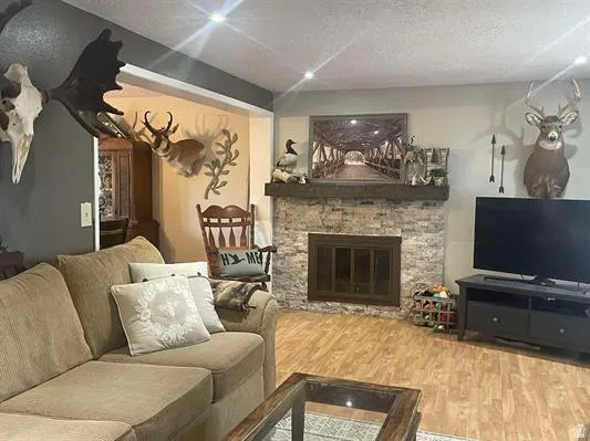Recessed lighting, wood-finish flooring, stone-clad fireplace with a dark wood mantel, and an open doorway