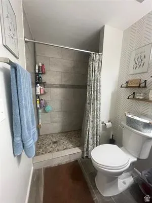 Walk-in shower with stone tile flooring and gray rectangular wall tiles, modern toilet, and decorative wall paneling