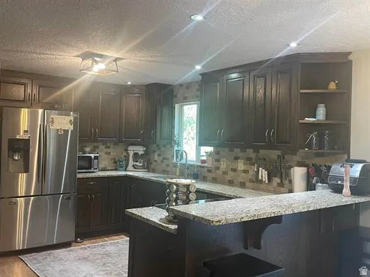 Dark wood-finish cabinetry, speckled granite countertops, stainless steel refrigerator, tile backsplash, and recessed lighting