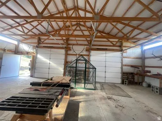 Exposed wood beam ceiling, concrete flooring, multiple overhead garage doors, built-in workbench, and an additional exterior door