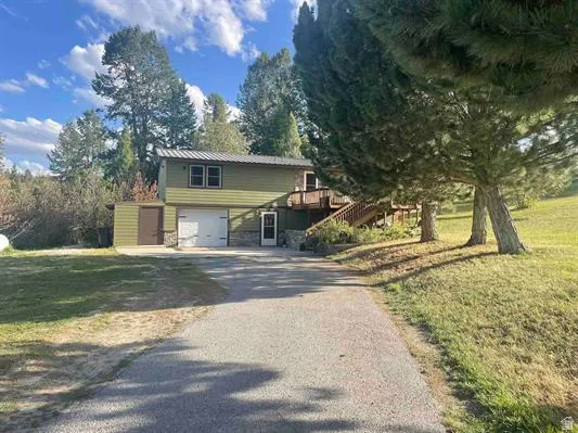 Two-story exterior with siding and stone accents, featuring an attached garage, an exterior staircase leading to a deck, and an additional shed