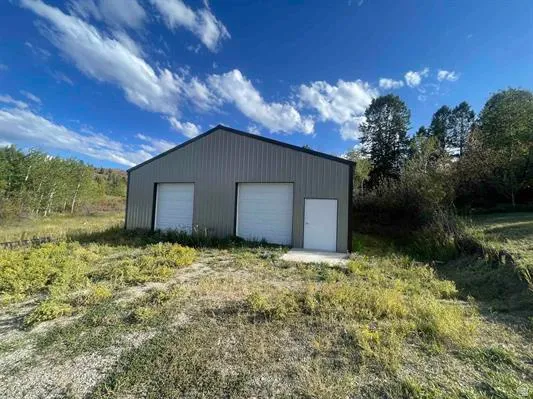 Metal-sided outbuilding featuring two garage doors and a separate entry door